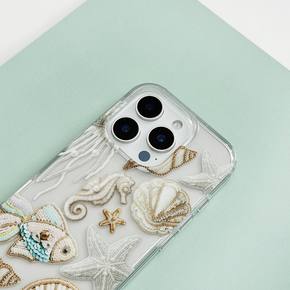 Clear phone case with embroidered shells, seahorse, starfish, and fish on a mint background.