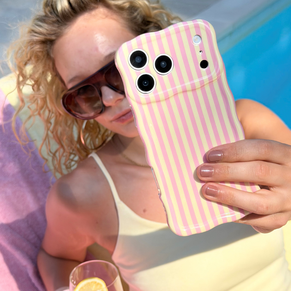 Woman holding a wavy pink lemonade phone with a pink and yellow striped case by a pool