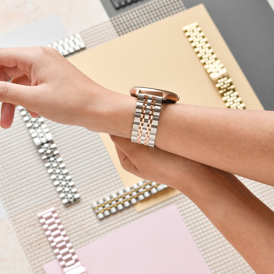 A person wearing a two-tone watch strap with a watch, showcasing multiple metal watch straps in various colors and designs on a flat surface.