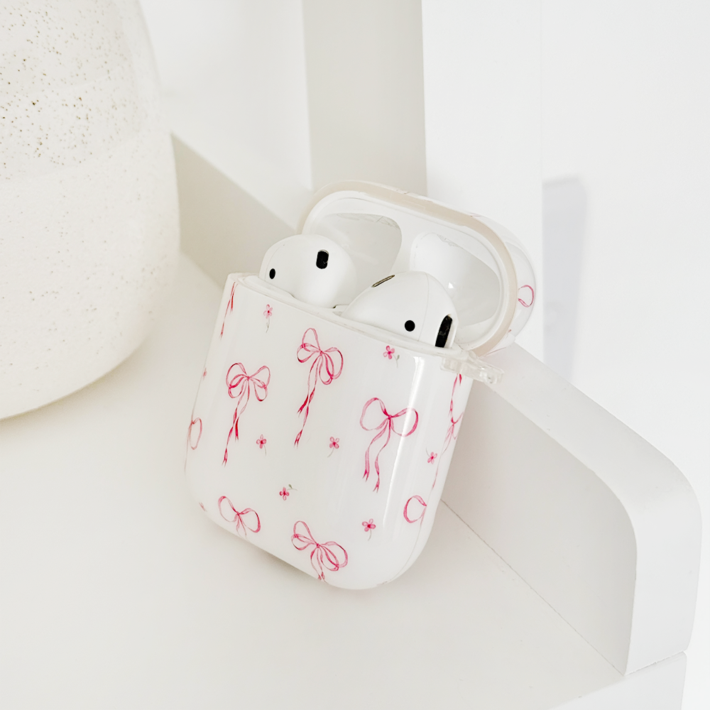 A hand with white-painted nails opens a pink case containing wireless earbuds against a beige background.
