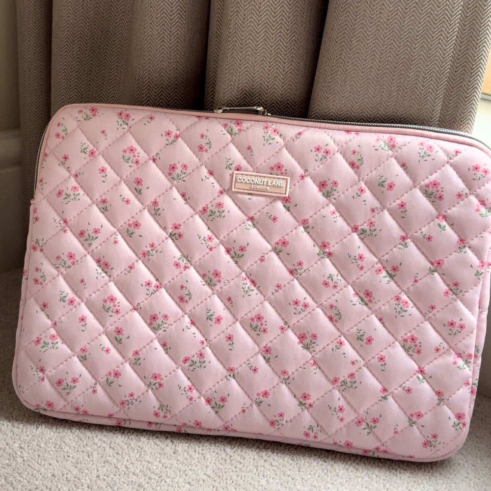 Coconut Lane pink quilted laptop sleeve with ditsy floral pattern, shown on a carpeted floor by beige curtains.