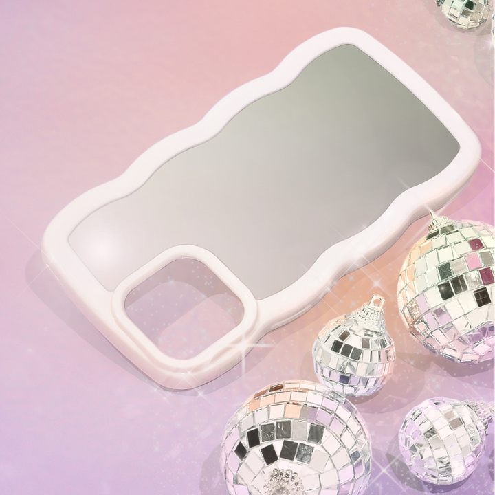 A sleek and stylish Curvy Mirror Phone Case - Cream from Coconut Lane lies on a pink and purple gradient background. Surrounding the curvy mirror phone case are several shiny, mirrored disco ball ornaments of varying sizes, reflecting light and casting a festive, glamorous feel to the image.