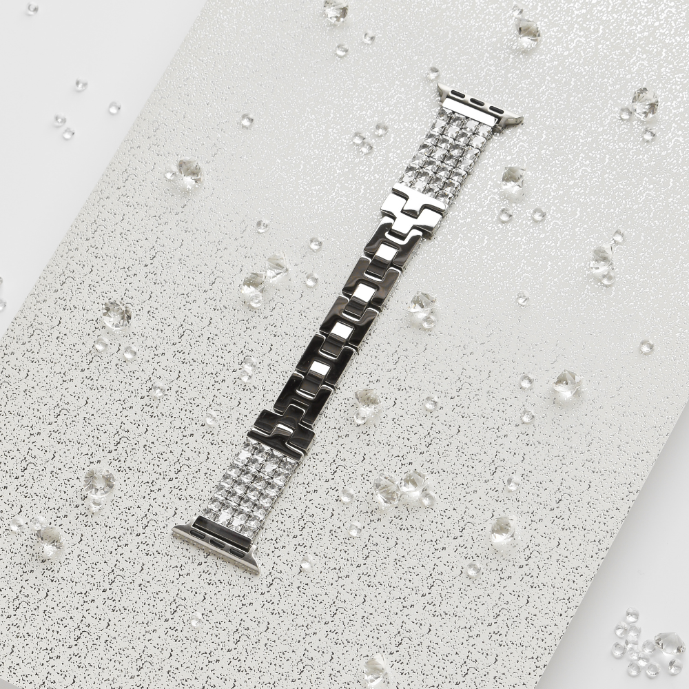 A Sparkle Super Glam Apple Watch Strap by Coconut Lane lies flat on a textured, glittery white surface. Small, reflective beads are scattered around, adding a touch of sparkle to the elegant and sophisticated presentation.