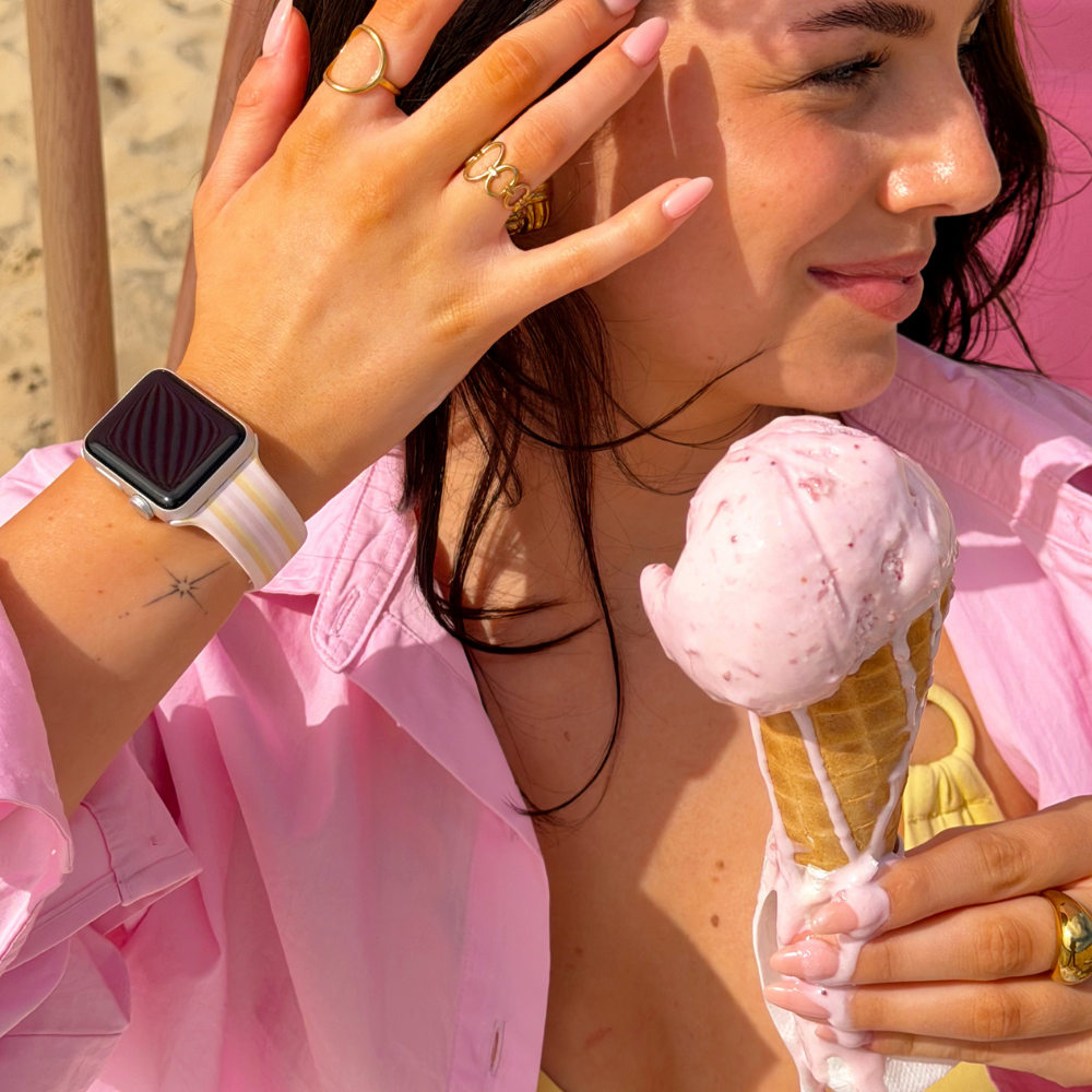Girl putting hair behind ear, holding an ice cream with her pastel stripes apple watch strap on her wrist