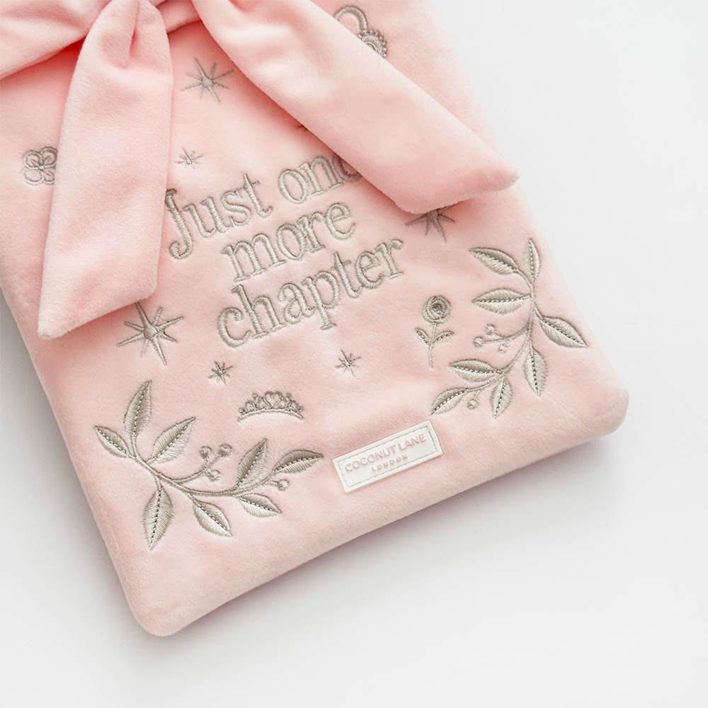 Book Sleeve made from soft blush pink velvet with grey embroidered floral details, stars and 'Just One More Chapter' lettering, finished with a large pink velvet bow and Coconut Lane logo, photographed on a white background.