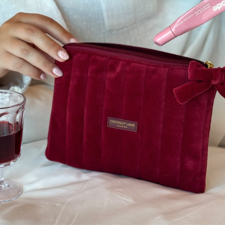 Burgundy velvet cosmetic bag with a quilted design, bow detail, and gold-tone hardware.