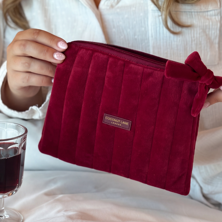 Burgundy velvet cosmetic bag with a quilted design, bow detail, and gold-tone hardware.