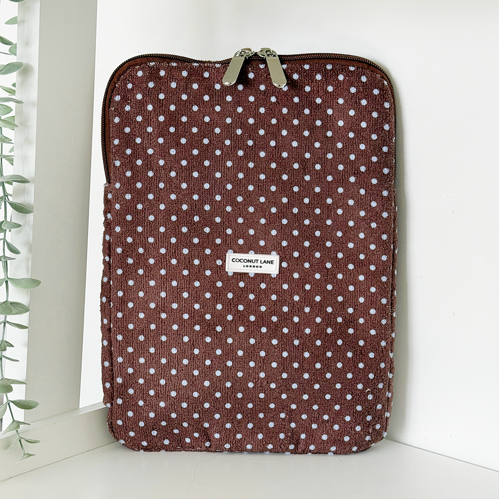 Brown and blue polka dot iPad sleeve by Coconut Lane standing upright on a shelf next to a leafy green plant.