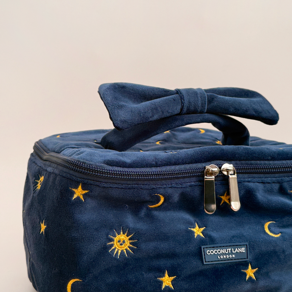 Navy blue travel vanity case with yellow stars and moons pattern, bow-shaped handle, and front label.