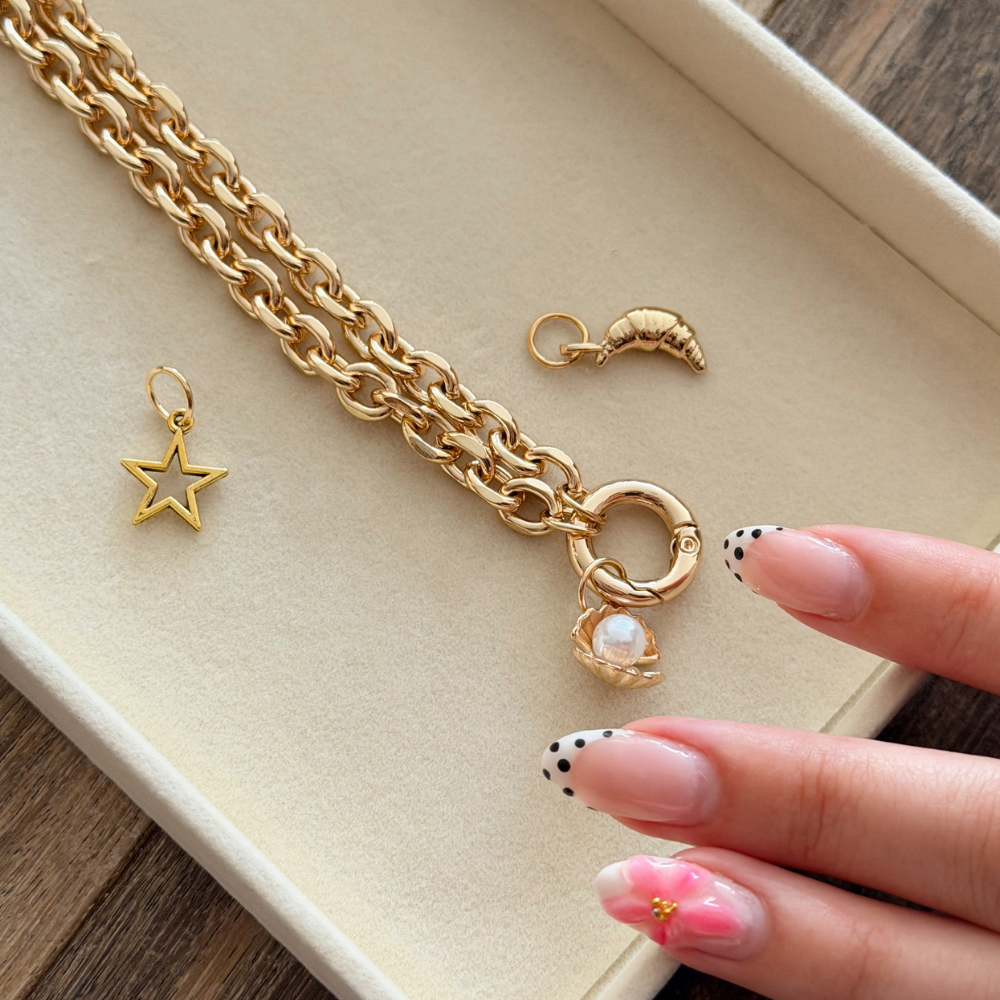 Gold jewelry set including a chain, star charm, and flower pendant on a wooden surface.