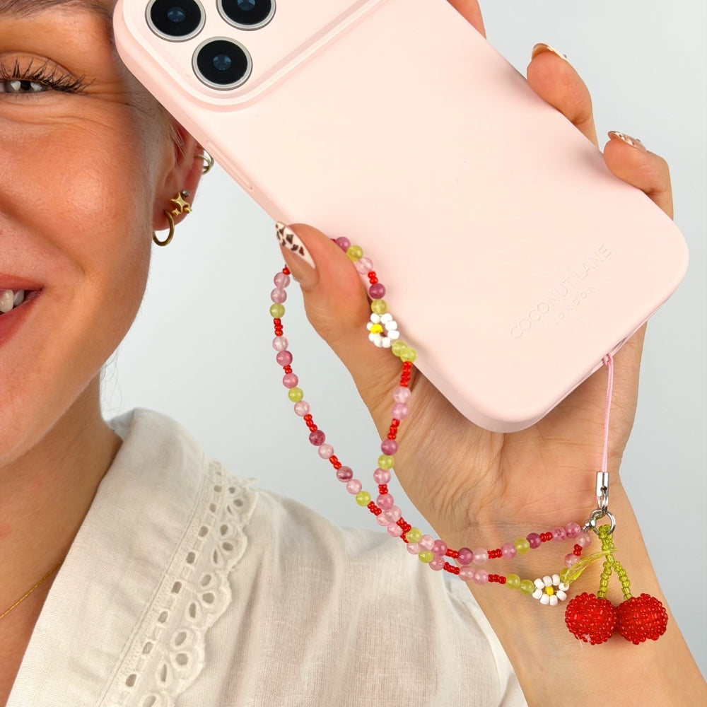 Person smiling holding a pink phone with a cherry bomb beaded phone strap