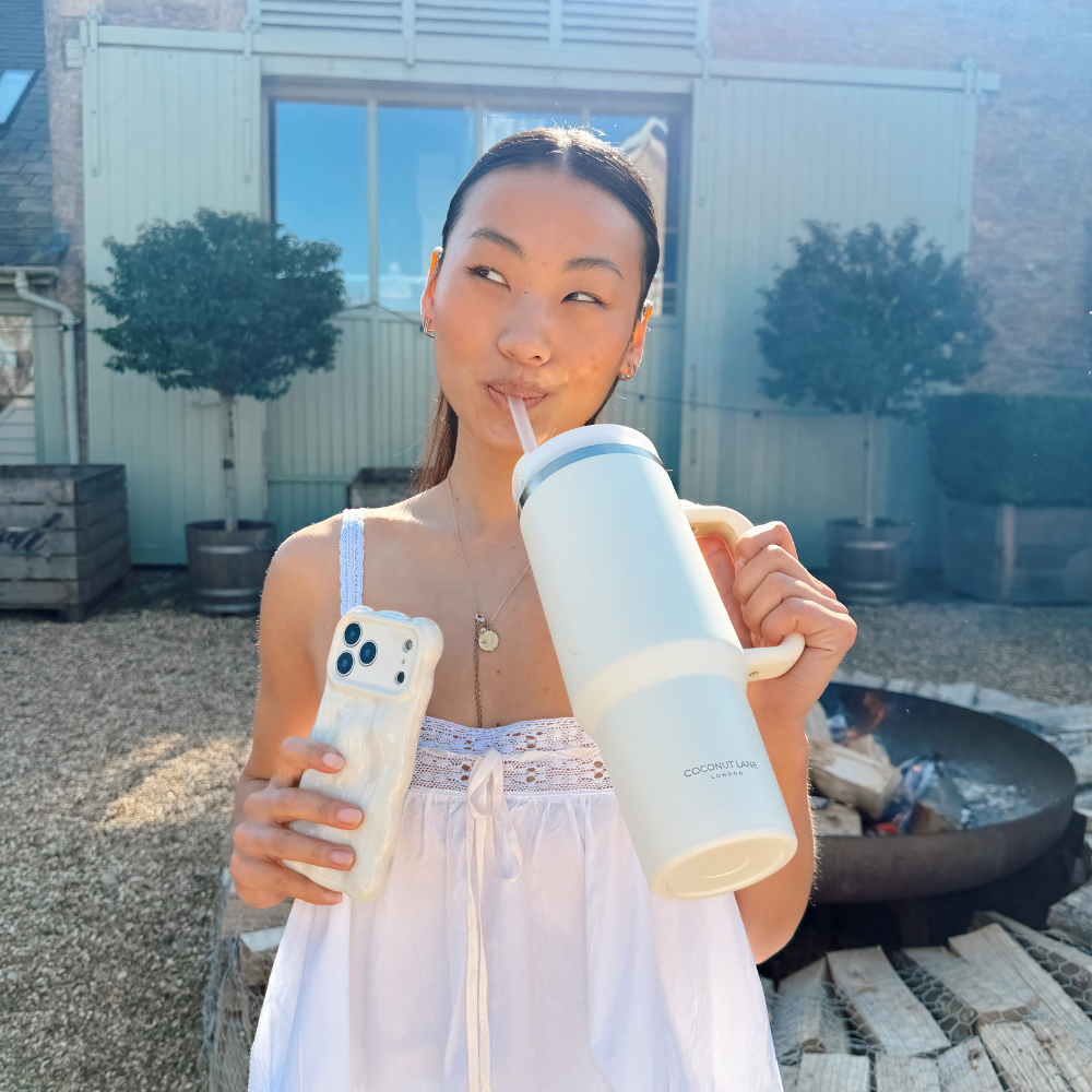 Girl sipping out of her cream stainless steel tumbler in front of a fire pit in spring time