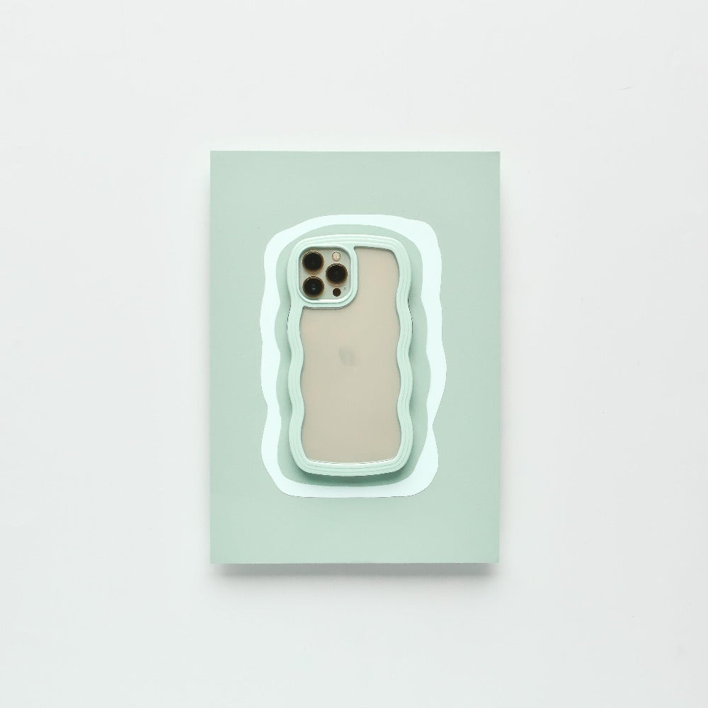 A modern iPhone 15 with a beige back and three camera lenses is placed on a pastel green rectangular surface. The surface features an irregular white and mint green outline, complementing the minimalistic setting. It is protected by the Mint Curvy Phone Case from Coconut Lane.