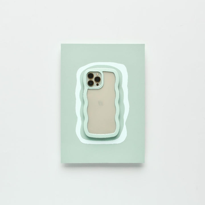A modern iPhone 15 with a beige back and three camera lenses is placed on a pastel green rectangular surface. The surface features an irregular white and mint green outline, complementing the minimalistic setting. It is protected by the Mint Curvy Phone Case from Coconut Lane.