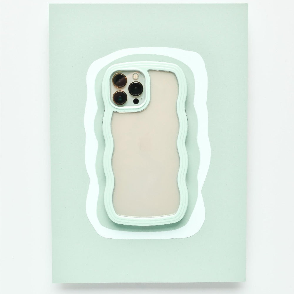 A mint green Curvy Phone Case - Mint by Coconut Lane with wavy edges holds an iPhone 15 featuring three cameras on the back. The protective case is set against a matching light green wavy background, creating a layered visual effect.