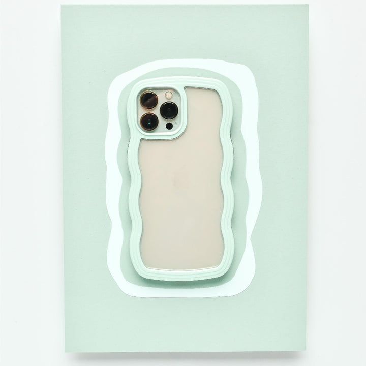 A mint green Curvy Phone Case - Mint by Coconut Lane with wavy edges holds an iPhone 15 featuring three cameras on the back. The protective case is set against a matching light green wavy background, creating a layered visual effect.