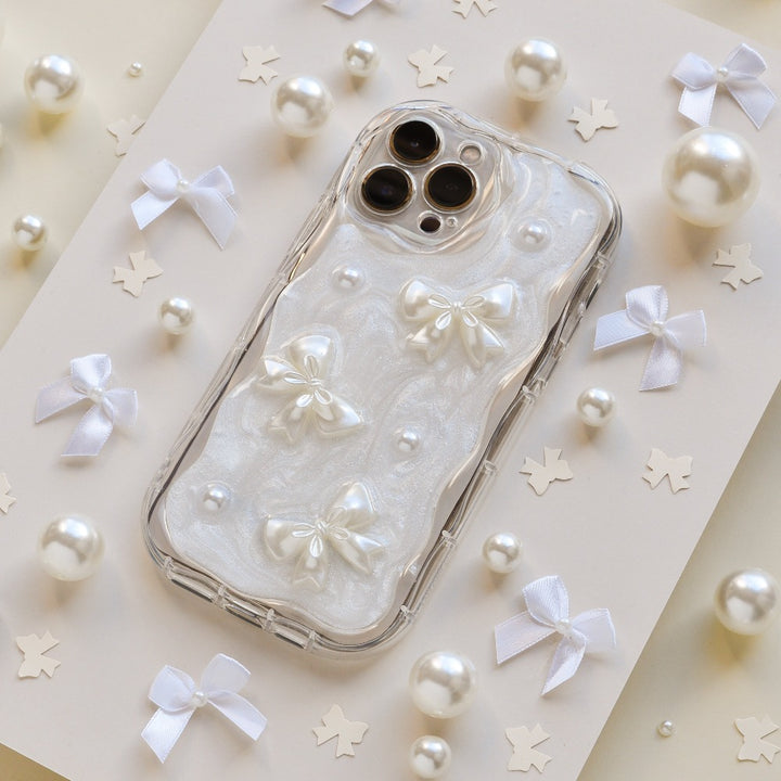 The Pearls & Bows Phone Case by Coconut Lane is adorned with white ribbon bows, pearls, and star-shaped confetti. This protective phone case showcases a pearlescent design featuring three 3D white bows and small pearl accents, all set against an elegant light-colored background.