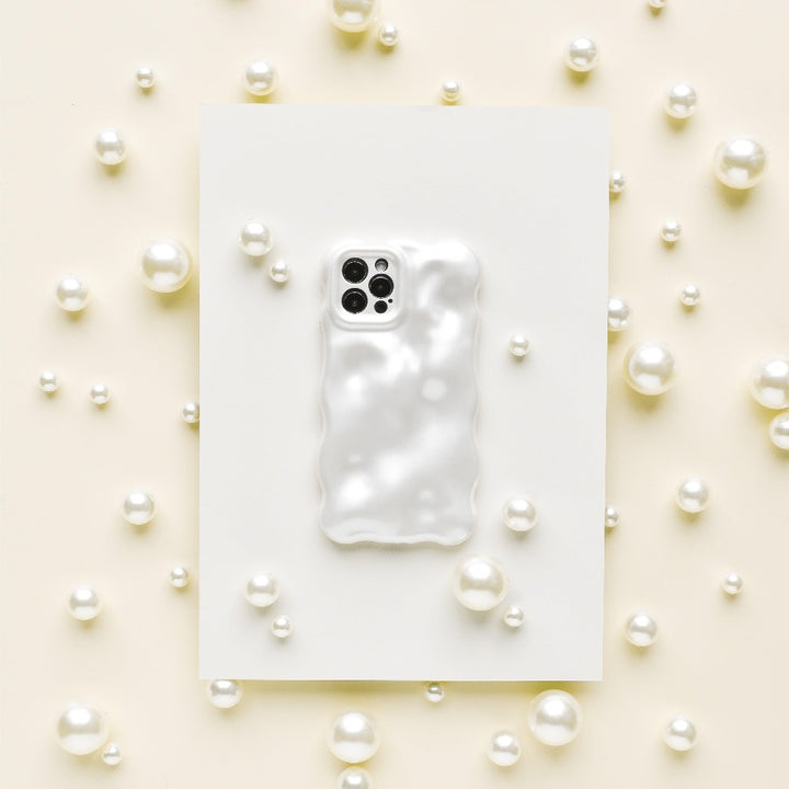 A Coconut Lane 3D Pearl Phone Case in white, featuring a glossy, wavy, pearl effect, is placed on a white rectangular sheet. The sheet is surrounded by various sizes of white pearls scattered on a light beige surface, creating an elegant and sophisticated display.