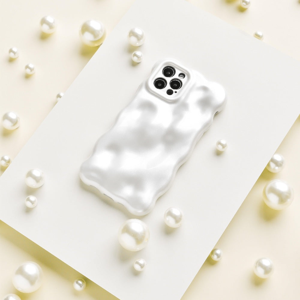 The 3D Pearl Phone Case - White from Coconut Lane, featuring a wavy texture and a glossy pearl white finish, is placed on a flat white surface surrounded by scattered pearls of various sizes. The case has precise openings for the camera and sensors at the top.