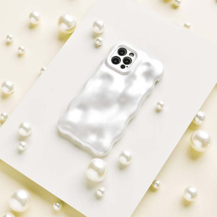 The 3D Pearl Phone Case - White from Coconut Lane, featuring a wavy texture and a glossy pearl white finish, is placed on a flat white surface surrounded by scattered pearls of various sizes. The case has precise openings for the camera and sensors at the top.