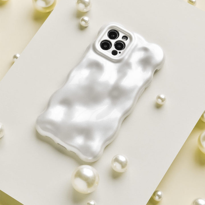 An iPhone with a glossy, ripple-patterned white case is displayed on a white rectangular surface. Surrounding the phone are scattered white pearls and Coconut Lane's 3D Pearl Phone Case - White, adding a touch of elegance to the composition.