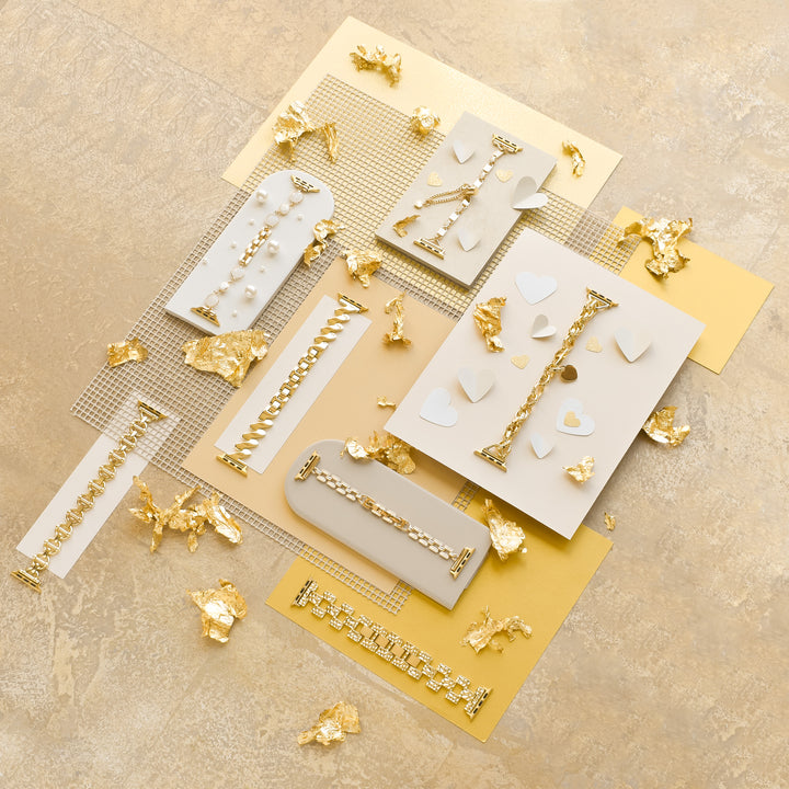 A collection of elegant gold and white polymer clay jewelry is displayed on beige and gold backgrounds, adorned with scattered gold flakes. The lineup features earrings, a stylish Square Gold Bracelet Apple Watch Strap by Coconut Lane, along with other pieces like square gold bracelets and pendants showcasing geometric designs, hearts, and braided patterns.