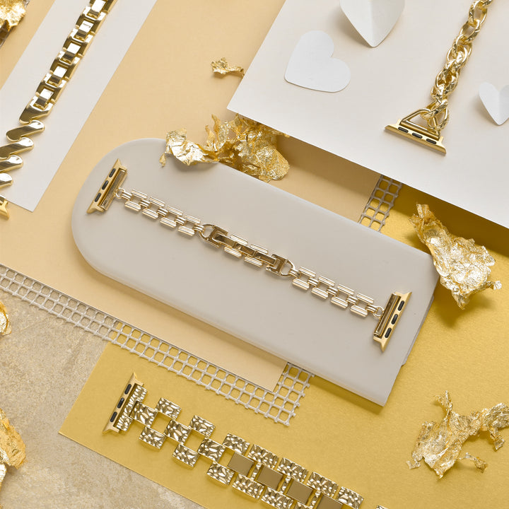 The image showcases a variety of gold chain bracelets from Coconut Lane, including the stunning Square Gold Bracelet Apple Watch Strap, all arranged on different textured backgrounds such as beige and white surfaces. Scattered gold foil accents enhance the aesthetic. The centerpiece is a prominent rectangular display featuring an elegant adjustable bracelet.
