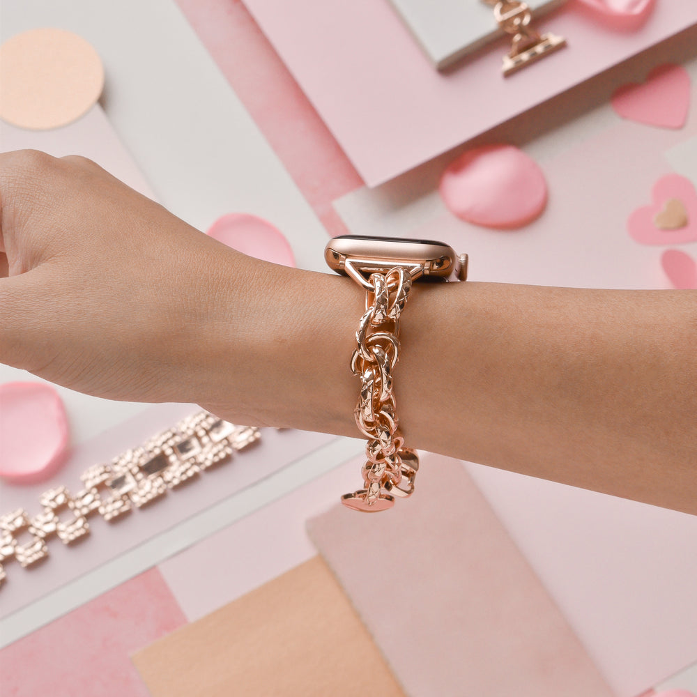 Close-up of a wrist adorned with the stylish Rose Gold Chain Bracelet Apple Watch Strap by Coconut Lane. The background showcases an array of pink and pastel-colored decorative elements, including hearts, circles, and rectangular shapes, creating a chic and feminine aesthetic reminiscent of this elegant accessory.