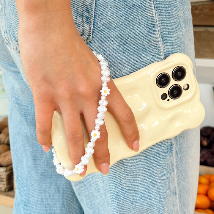 Girl next to fruit stand with phone case and Daisy Pearl phone strap attached