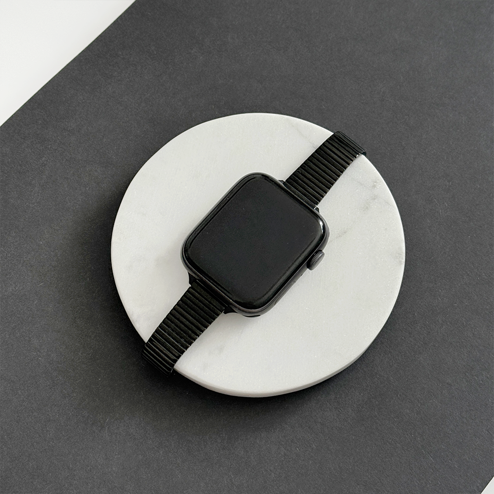 Black SLIM Fine Line Apple Watch strap by Coconut Lane displayed on a white stone with a black background.