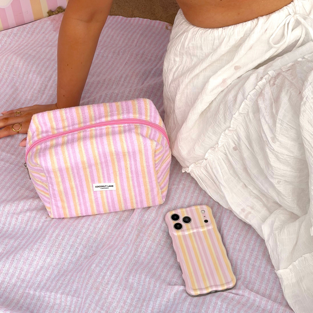 Girl laying on her towel on the beach next to towel makeup bag in pastel stripes and matching wavy phone case