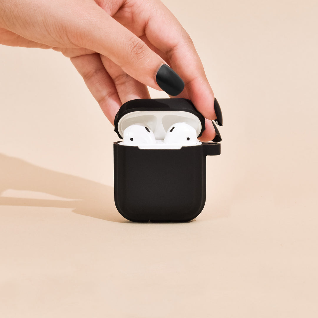 Black wireless earbuds case with white earbuds held by a hand on a beige background