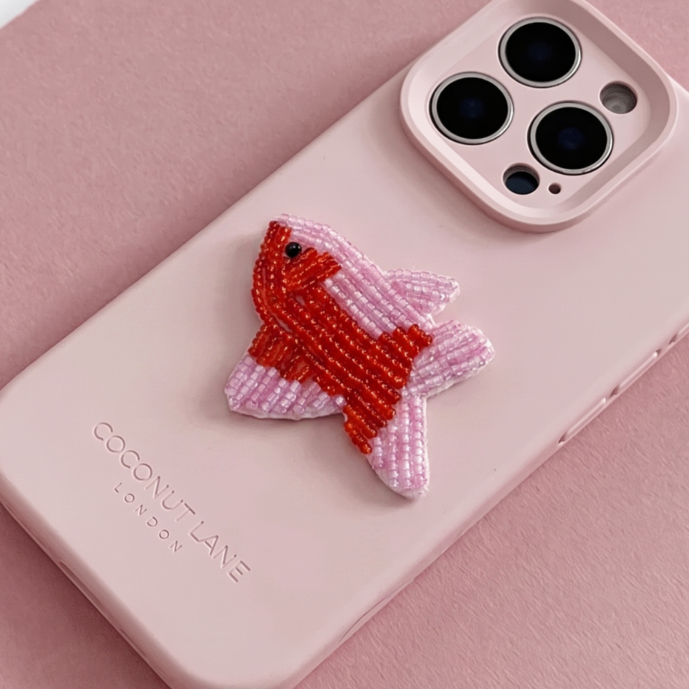 Red and pink 3D fish made from beads and sequins, on top of a pink Coconut Lane Phone Case. 