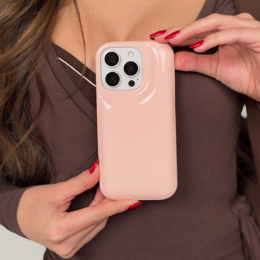 Woman in a brown pilates outfit is holding an iphone in a glossy pastel pink Coconut Lane puffer phone case with embossed logo, 