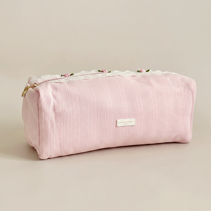 Pink pointelle fabric hair tool bag with Coconut Lane logo badge. White lace trim detailing.