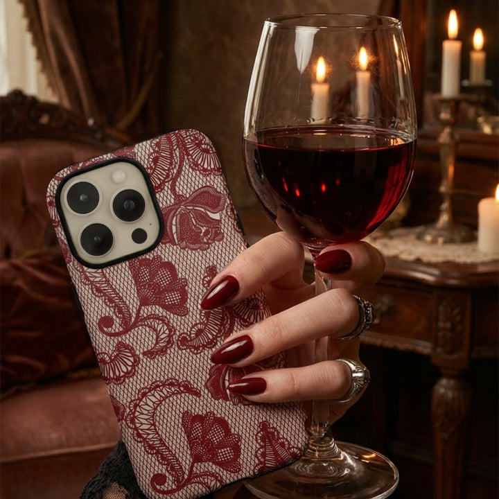 Hand holding a phone case with lace design and a glass of red wine in a cozy setting.