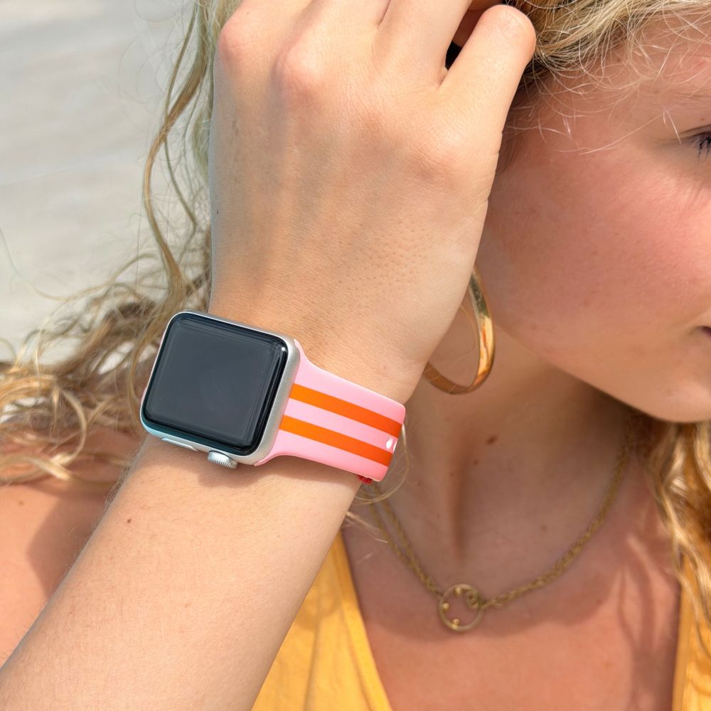 Person wearing a pink & orange striped watch band on a beach