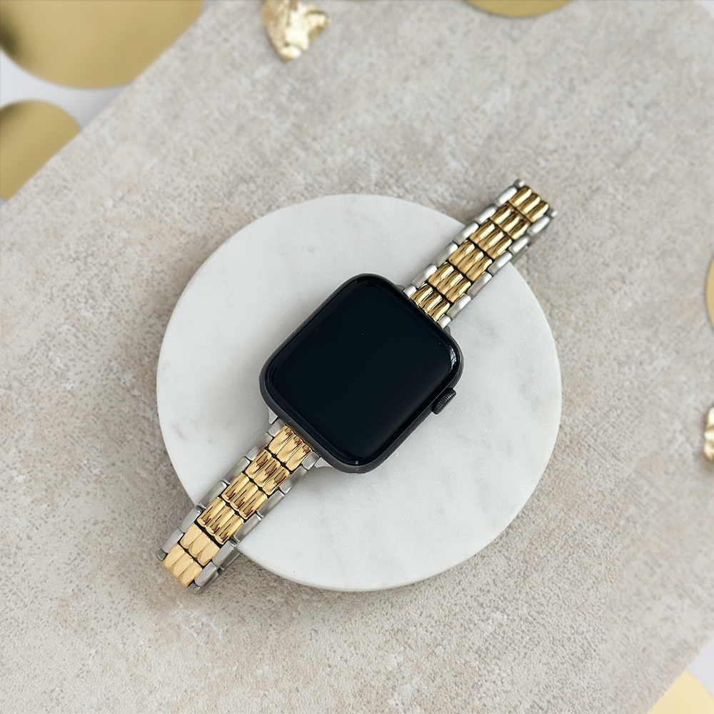 Coconut Lane retro slim two-tone stainless steel Apple Watch strap displayed on a round marble stand.