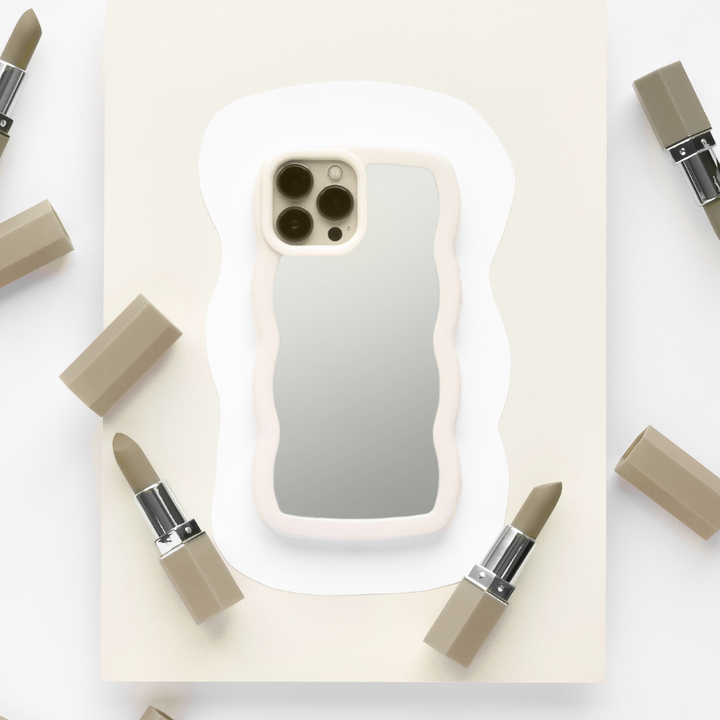 A sleek and stylish iPhone adorned with the Coconut Lane Curvy Mirror Phone Case in Cream is centered on a piece of off-white paper. The phone's camera is visible, reflecting off the back of the case. Surrounding the device are six muted beige lipsticks, some with their caps removed, arranged in a circular pattern.