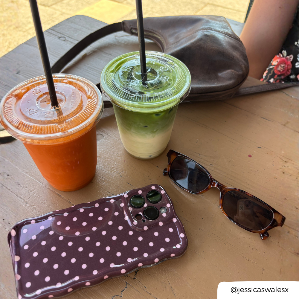 a table with an iced matcha and smoothie, with an iphone placed down. The iphone has a brown with light pink polka dots phone case. 