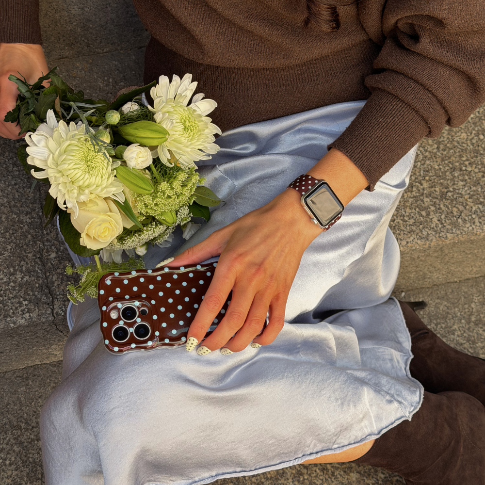 Girl sat on step holding flowers and brown and blue polka dot phone case