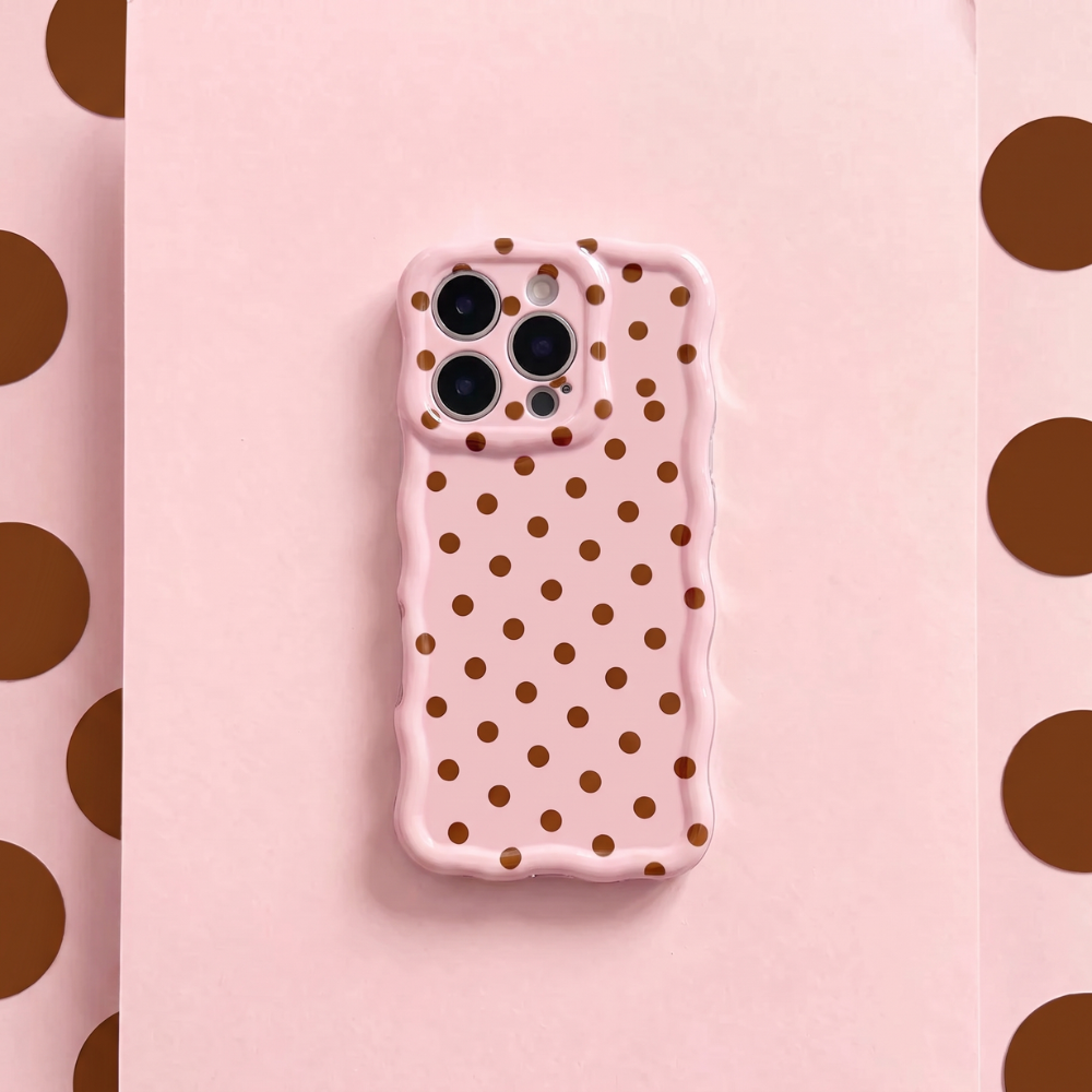 Pink Wavy Phone Case featuring a glossy blush pink finish with brown polka dots, scalloped edges and triple camera cutouts, displayed on a matching pink background.