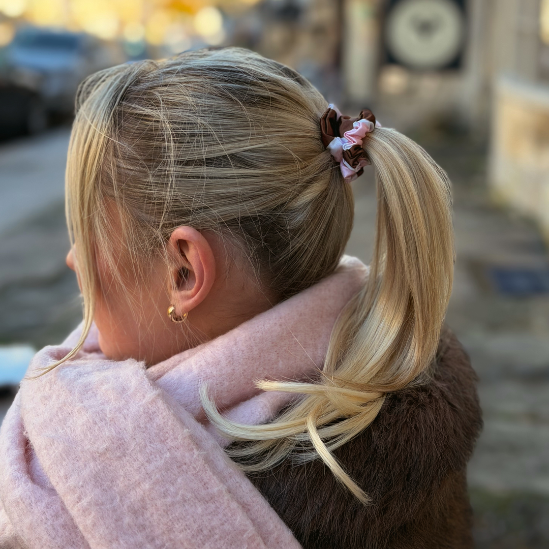 Woman with blonde hair wearing a Satin hair scrunchie in a brown, pink and white striped design.