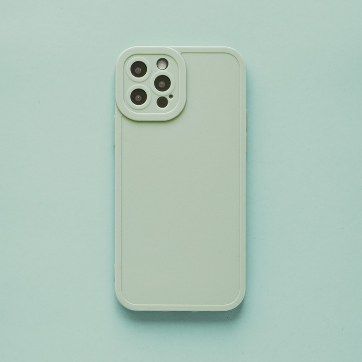 A Coconut Lane NAKD Phone Case in Sage is displayed on a coordinating light green background, encasing a light green smartphone. The back offers comprehensive camera protection for three lenses and a flash arranged in a triangular formation at the top left corner.