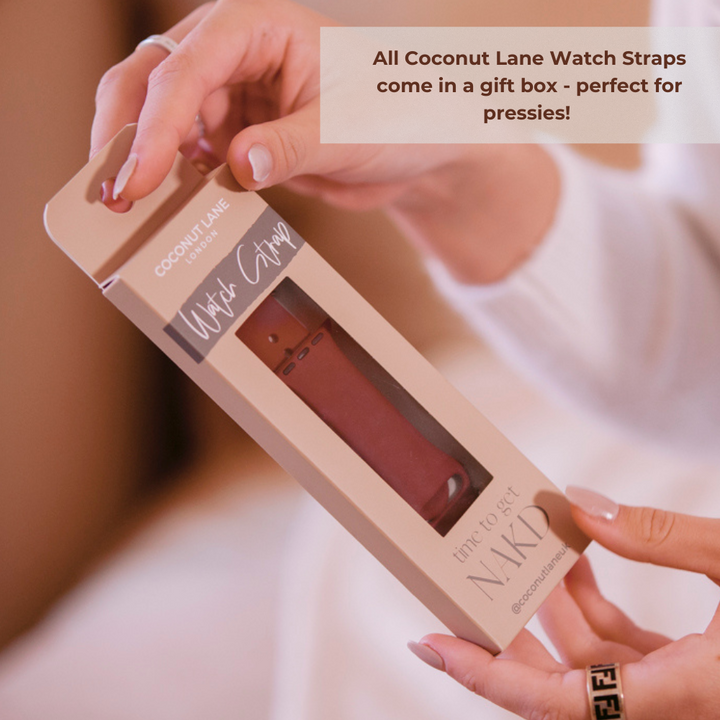 A person is holding a boxed Coconut Lane NAKD Apple Watch Strap in Cool Mint. The packaging reads "time to get NAKD." A text overlay in the image states, "All Coconut Lane Watch Straps come in a gift box - perfect for pressies!" The person's nails are painted white, and they wear a ring.