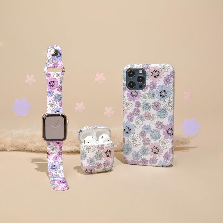 A coordinated tech accessory set in a floral design, featuring Coconut Lane's Pastel Flowers Apple Watch Strap with a matching band. The set also includes wireless earbuds in a floral case and phone cases adorned with similar floral patterns on a beige background with scattered flower cut-outs.