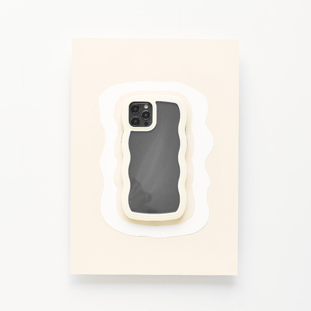 A highly protective Coconut Lane Curvy Phone Case - Cream, featuring a wavy design, is placed centrally on a rectangular surface layered to resemble paper cut-outs in various shades of white. The screen of the iPhone 15 is off, reflecting light slightly.