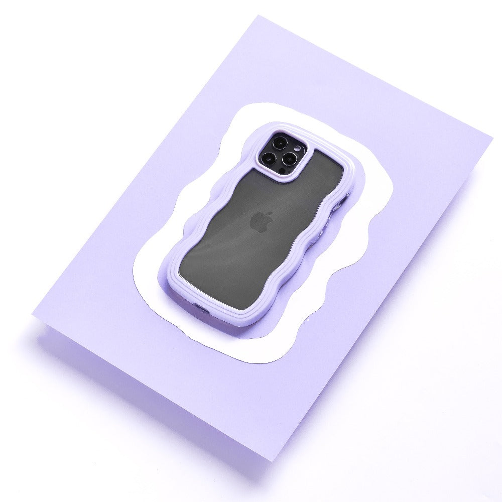 The iPhone15, featuring a dark screen, is enclosed in the Curvy Phone Case - Lilac from Coconut Lane. This highly protective case with stylishly scalloped edges adds a decorative touch as it sits on a light purple paper background.